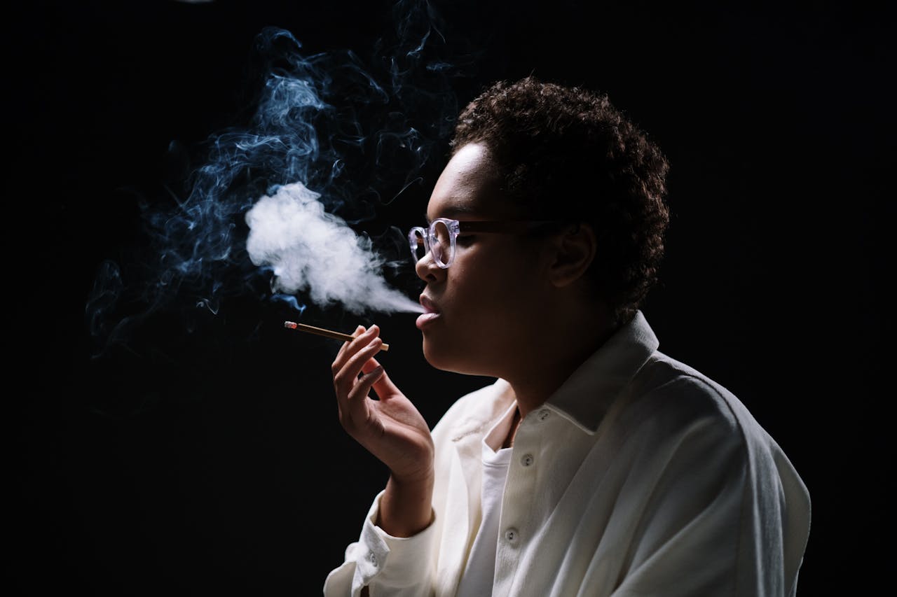 mobile-02 Close-up of a woman in glasses exhaling smoke against a dark background.