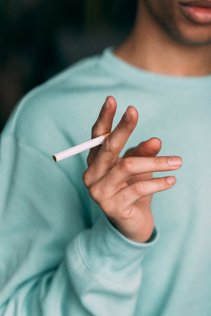Mastering the First Impression: Your intriguing post title goes here A young man holding an unlit cigarette indoors, emphasizing lifestyle choices and casual style.