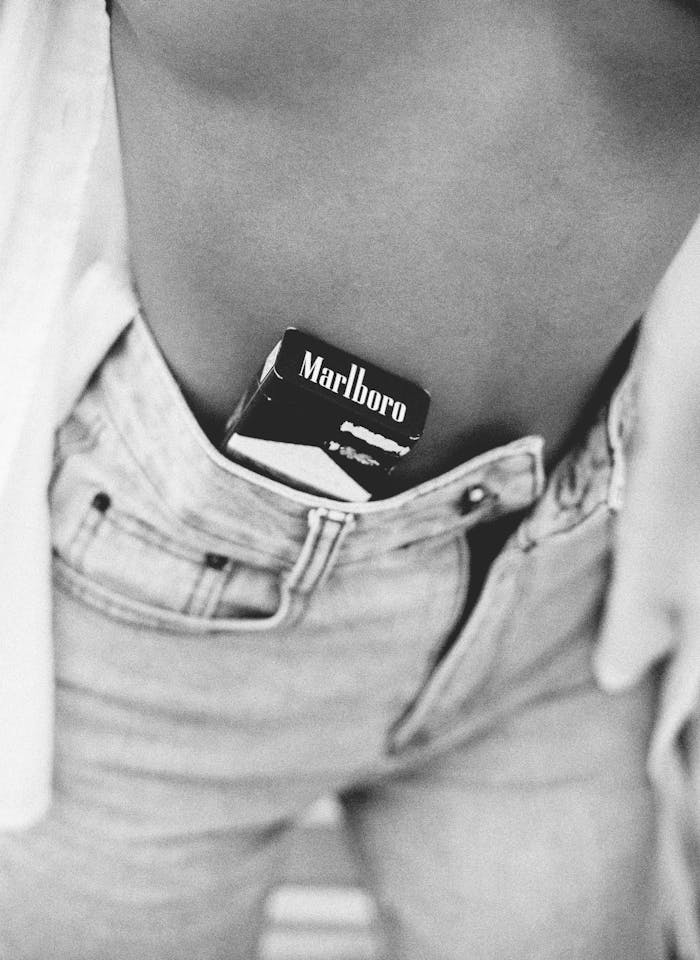 A monochrome photo featuring a cigarette pack tucked into denim jeans, emphasizing fashion and lifestyle.